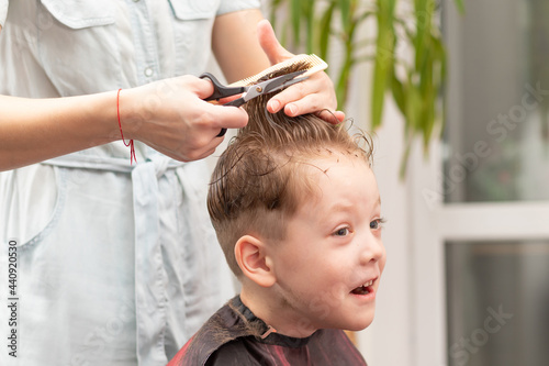 caring female hands of a mother with a comb and scissors make a fashionable haircut for her son at home during the second lockdown. selective focus photo