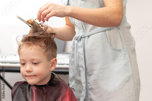 caring female hands of a mother with a comb and scissors make a fashionable haircut for her son at home during the second lockdown. selective focus