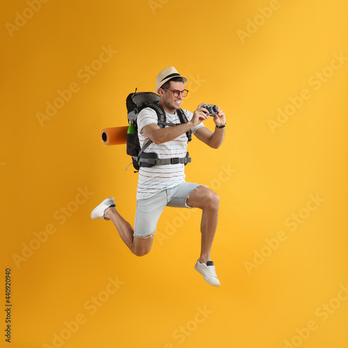 Male tourist with travel backpack taking picture on yellow background