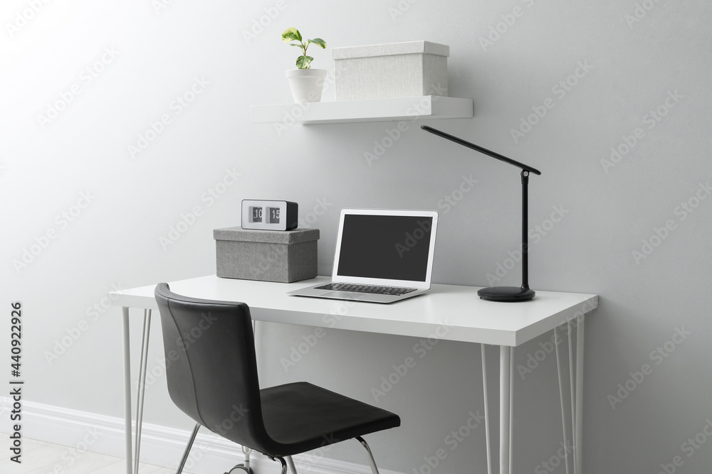Stylish workplace with laptop and comfortable chair near white wall indoors. Interior design Stylish workplace with laptop and comfortable chair near white wall indoors. Interior design
