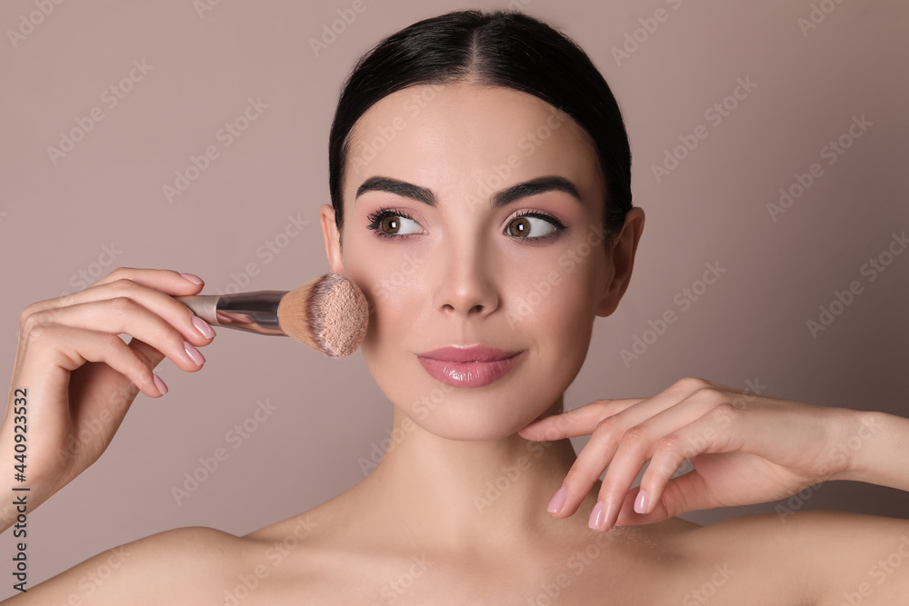 Beautiful young woman applying face powder with brush on dusty rose background Beautiful young woman applying face powder with brush on dusty rose background