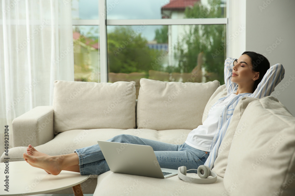 Young woman with laptop and headphones relaxing on sofa at home, space for text Young woman with laptop and headphones relaxing on sofa at home, space for text
