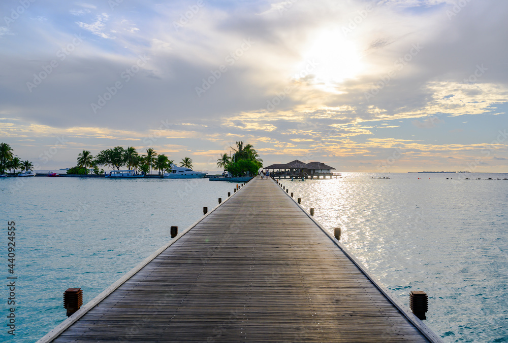 Fototapeta premium Boats, palm trees and a wooden pier stretching out into the ocean under the evening cloudy sky