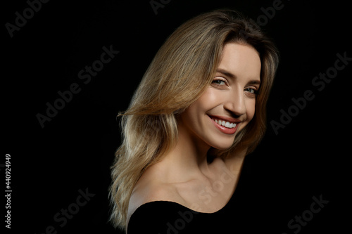 Portrait of happy young woman with beautiful blonde hair and charming smile on black background