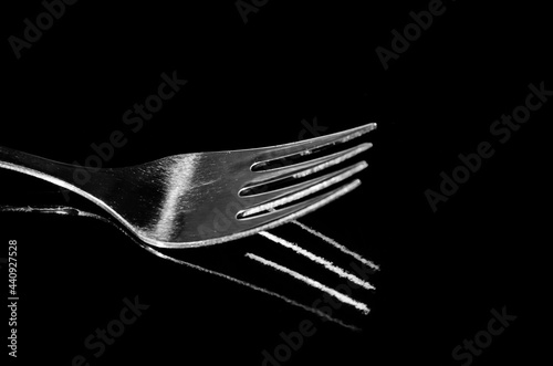 Close-up of a fork horizontally on a black surface, shadow reflection