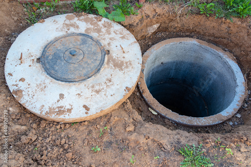 a well made of concrete rings and a cover with a plastic hatch. Home drainage system construction. Sanitary septic tank