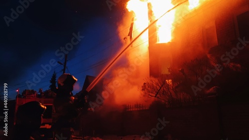 The roof of the house is on fire. The residential building burn, village. Firefighters put out a fire from the crane from above. The fire Department putting out the open flame. Smoke and sparks. photo