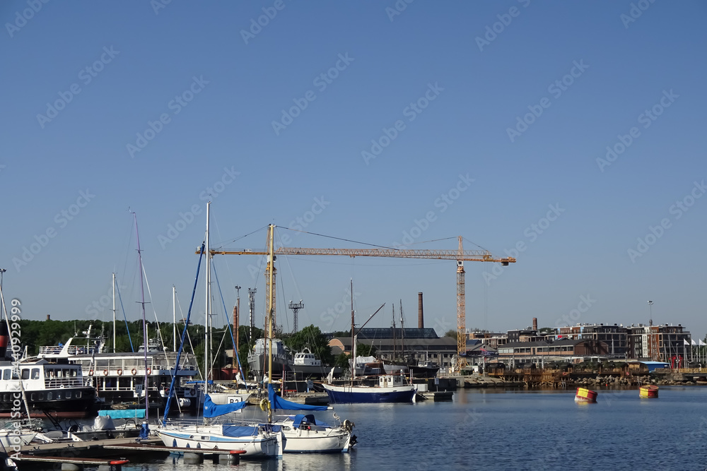 Seascape with yachts and boats in Noblessner port. Modern building on the back. Two yellow high cranes. Modern buildings on the back. Blue clear sky on a sunny summer day. Tallinn, Estonia