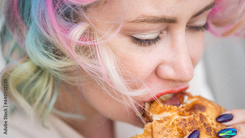 Caucasian woman with curly colored hair eating burger. Bad eating habits and love of fast food Caucasian woman with curly colored hair eating burger. Bad eating habits and love of fast food