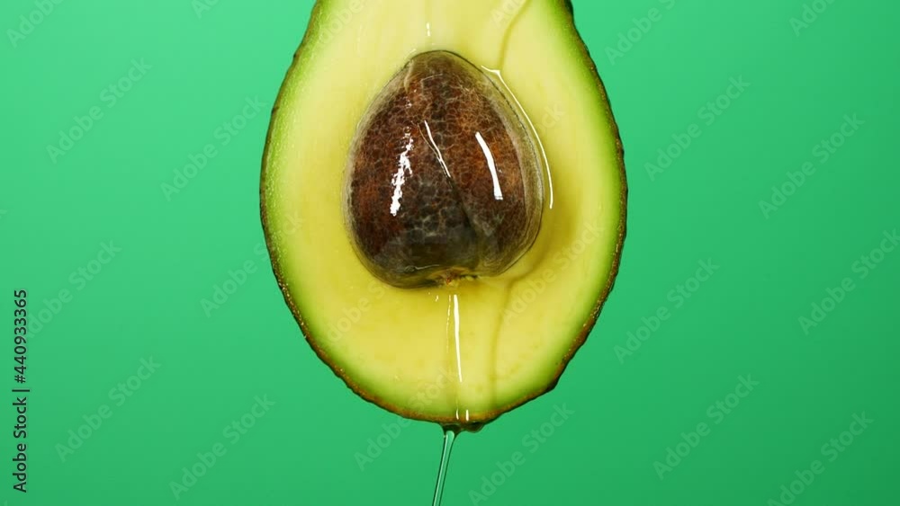 Slow motion of oil liquid splasing from fresh avocado fruit on green background
