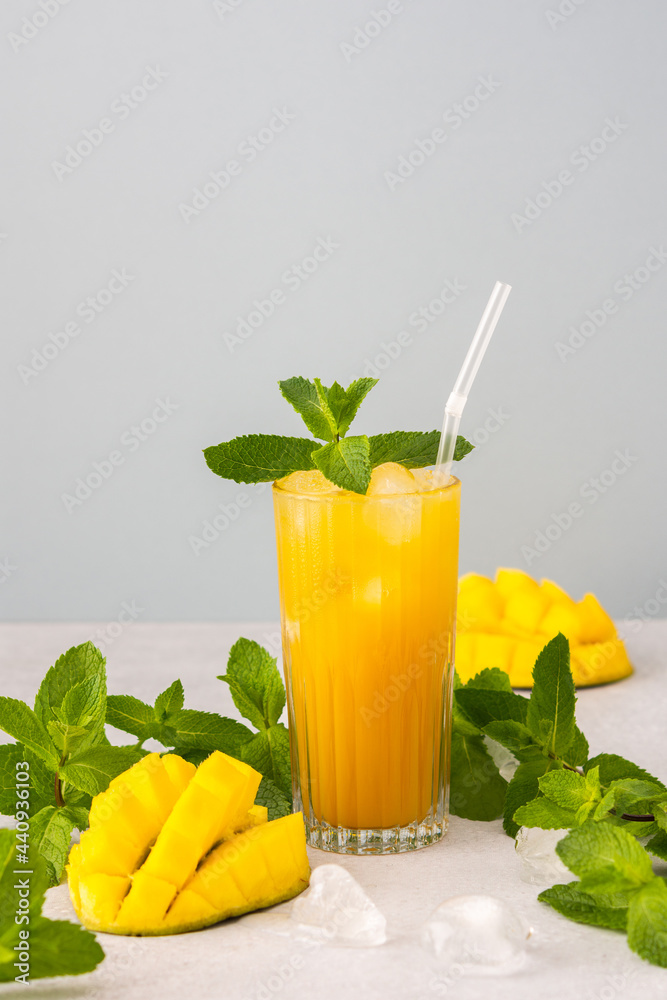 Freshly squeezed mango juice with ice in glass with a straw, ripe cut mango with mint on a gray background Freshly squeezed mango juice with ice in glass with a straw, ripe cut mango with mint on a gray background