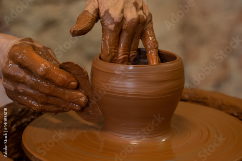Old woman potter working on Potter wheel making a clay pot. Master forming the clay with her hands creating pot in a workshop