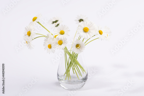 Small daisy flowers in glass vase isolated on white background.