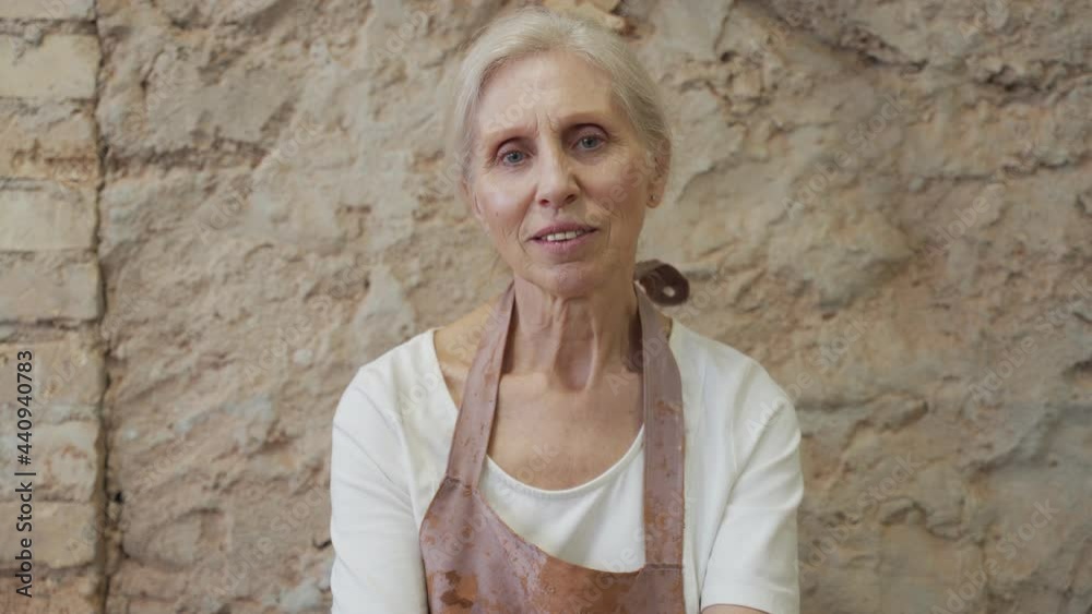 Portrait of an elderly female potter, sitting in a pottery workshop and looking at the camera Portrait of an elderly female potter, sitting in a pottery workshop and looking at the camera