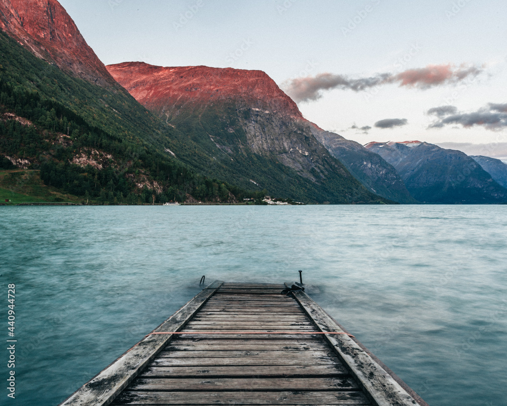 Stairs leading to a lake in the water surrounded by mountains and a red sunset