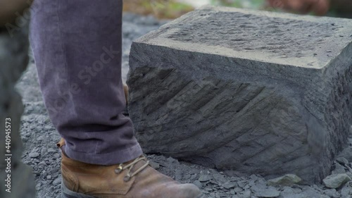 Handheld dolly shot of a stone craftsman using a pick to edge a large stone brick, in the city of Ancud, on the island of Chiloe. photo