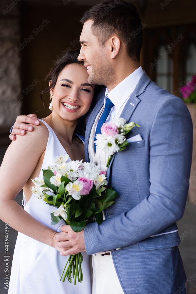 Happy groom hugging bride with bouquet outdoors Happy groom hugging bride with bouquet outdoors