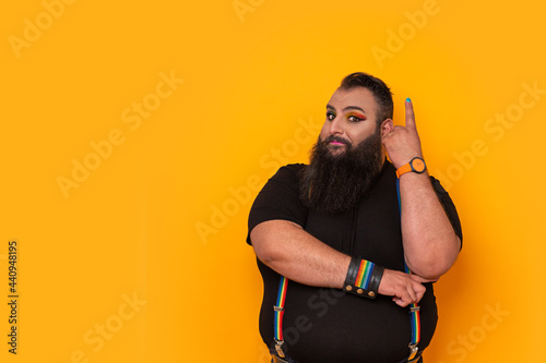 Bearded gay big man with rainbow trouser holder and make-up pointing up photo