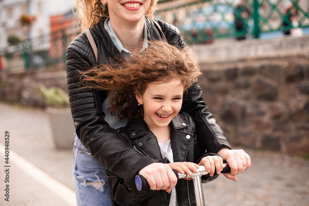 Obraz premium Mom and daughter ride a scooter and have a great time