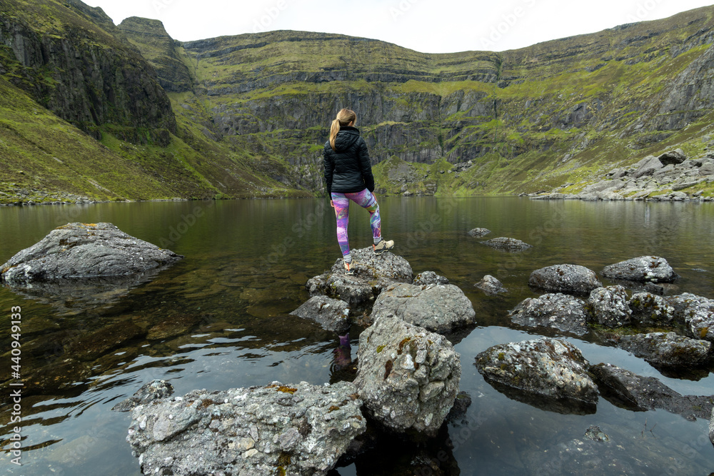 Woman standing on stones at Coumshingaun Lake Ireland