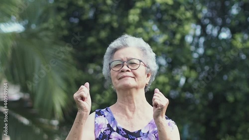 Senior woman with short gray hair hands up exercise while standing in a garden. Aged people and healthcare concept.