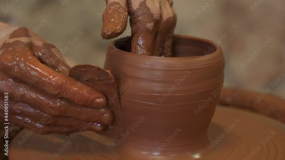 Old woman potter working on Potter wheel making a clay pot. Master forming the clay with her hands creating pot in a workshop