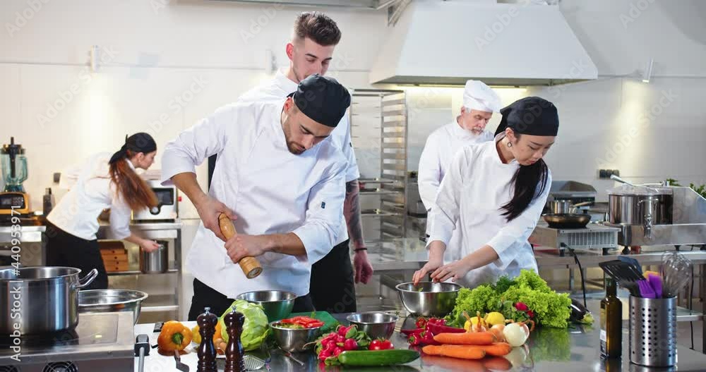 Workflow in cafeteria kitchen. Busy mixed-race team of chefs preparing food in famous restaurant. Caucasian young man cook preparing meal in restaurant with Asian woman colleague, culinary concept Workflow in cafeteria kitchen. Busy mixed-race team of chefs preparing food in famous restaurant. Caucasian young man cook preparing meal in restaurant with Asian woman colleague, culinary concept