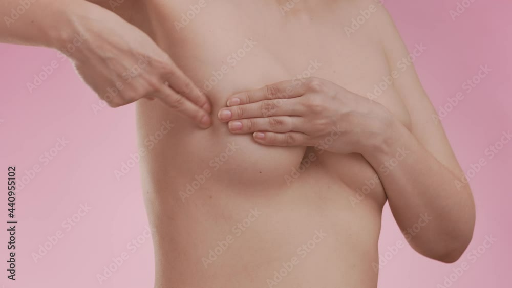 Breast cancer awareness. Young topless woman doing breast self-exam (BSE) on pink background. Checking up breast changes, possible lumps, distortions or swelling. Healthcare and medical concept. Breast cancer awareness. Young topless woman doing breast self-exam (BSE) on pink background. Checking up breast changes, possible lumps, distortions or swelling. Healthcare and medical concept.