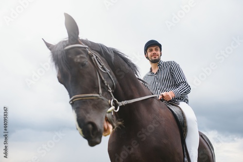Beautiful man riding a horse on field at summer