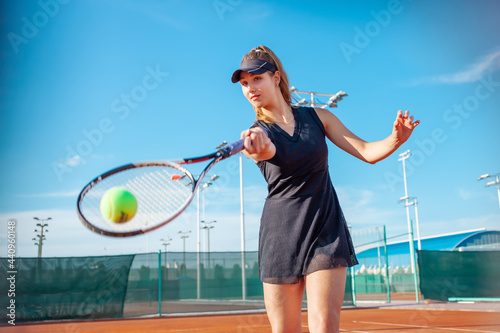 A beautiful woman plays tennis on the court. Sunlight, training, competition. Outdoor sports, team play. Active lifestyle, athlete with a racket and a ball. portrait
