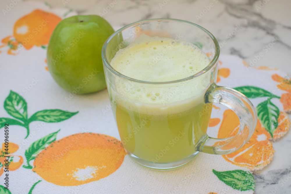 Freshly squeezed apple juice. A mug of apple juice stands on the table, with a green apple in the background Freshly squeezed apple juice. A mug of apple juice stands on the table, with a green apple in the background