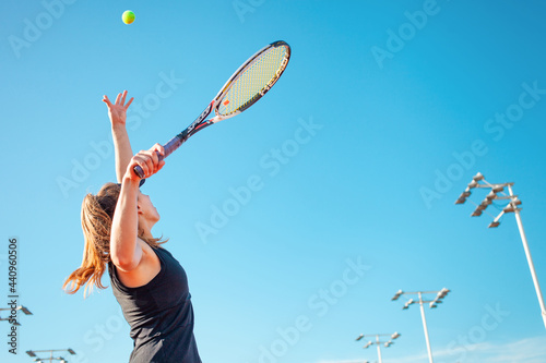 A beautiful woman serves the ball. Tennis court, sunlight. The girl in the black suit dress. A sporty lifestyle in the open air. A professional athlete trains. copyspace