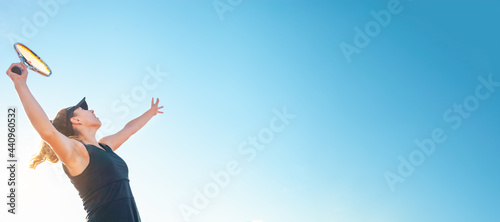 A beautiful woman serves the ball. Tennis court, sunlight. The girl in the black suit dress. A sporty lifestyle in the open air. A professional athlete trains. banner copyspace