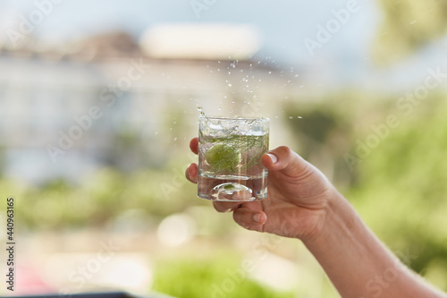 Man holds in his hands a glass of homemade cocktail of hard seltzer with herbs in front of mountains. Summer wallpaper close up.