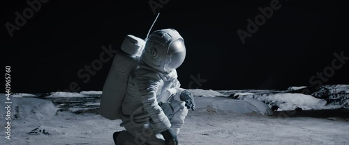 CU Portrait of Caucasian female lunar astronaut finds something and kneels while exploring Moon surface. Shot with 2x anamorphic lens