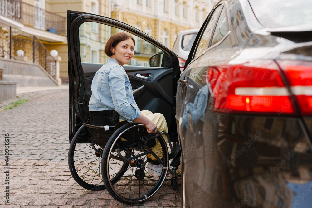 Brunette woman smiling and sitting in wheelchair by car on city street Brunette woman smiling and sitting in wheelchair by car on city street