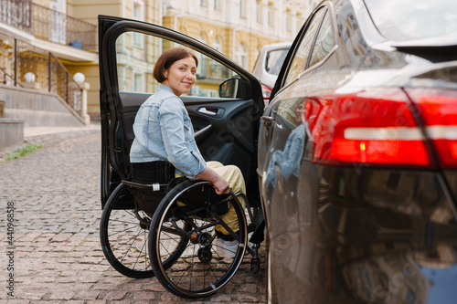 Brunette woman smiling and sitting in wheelchair by car on city street