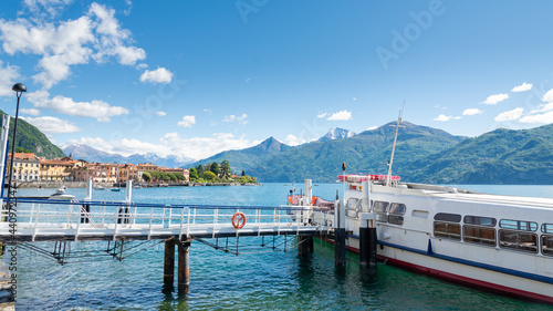 Gangway leading to a ferry-boat at the small harbour of Menaggio, Lake Como, Italy. Italian alps mountain range, with blue sky and clouds on the background. © Travelling Jack