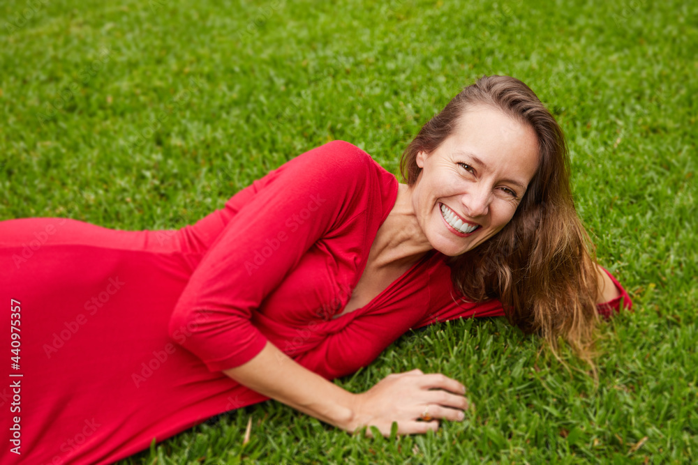 Woman dressed in red lying on the ground in a park with grass Woman dressed in red lying on the ground in a park with grass