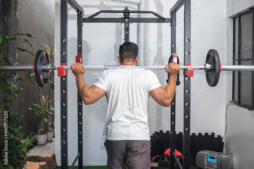 A fit asian man prepares to do barbell back squats at his home gym. Leg workout and training routine. photo