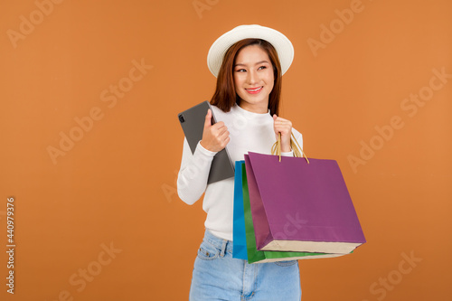 A beautiful Asian woman wearing a white long sleeve sweater and jeans, carrying a paper bag with items bought and tablet from a department store.