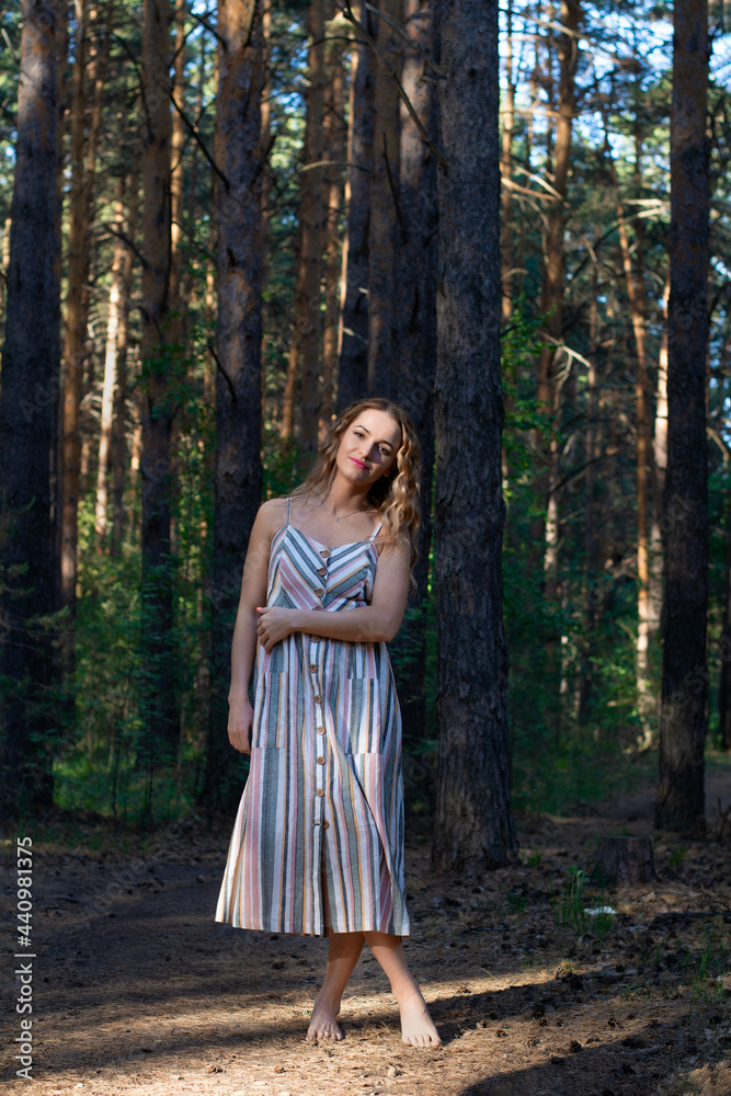 curly blonde woman in a dress walks in a pine forest