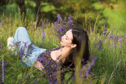 Young relaxed girl enjoys rest lying among wildflowers and grass on a sunny day in a meadow.	
