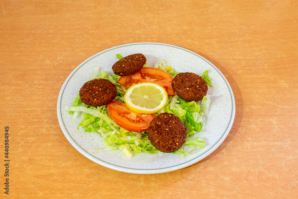 Ration of slices of falafel battered with tomato and lettuce salad served in a European Pakistani restaurant on a round plate Ration of slices of falafel battered with tomato and lettuce salad served in a European Pakistani restaurant on a round plate