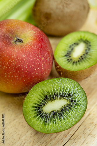Close-up of kiwi cut in half and more kiwis in the background with red apple on light wooden background