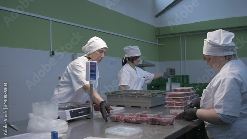 Female workers in black proective gloves prepare fresh meat for delivery to stores. Slow motion. Meat production and food industry, photo