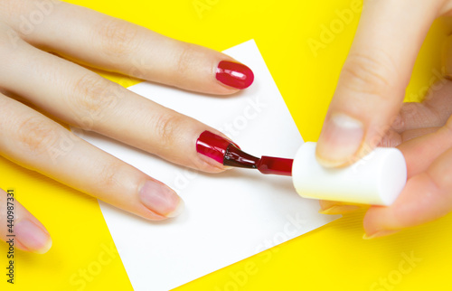 Woman applies red nail polish on the yellow background..Girl making a manicure. Salon procedures at home. Beautiful hands and nails. Close up  macro photo. Colorful and creative.