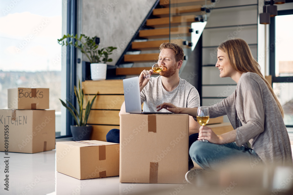 Young couple using laptop and drinking wine after moving in their new home. Young couple using laptop and drinking wine after moving in their new home.