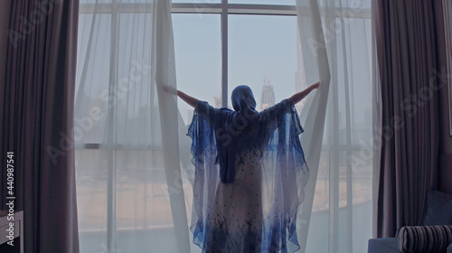 Photography Back view of woman opening curtains and looking out of window to cityscape at hotel in the morning