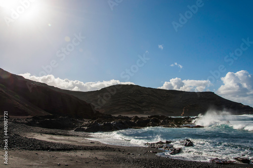 Kanaren, Lanzarote,. Küstenlinie mit typischen schwarzem Strand und kräftiger Brandung. Im Hintergrund die typische vulkanische Landschaft